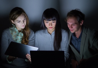 Group of people looking at laptop screen in dark room (© chombosan / Fotolia.com)